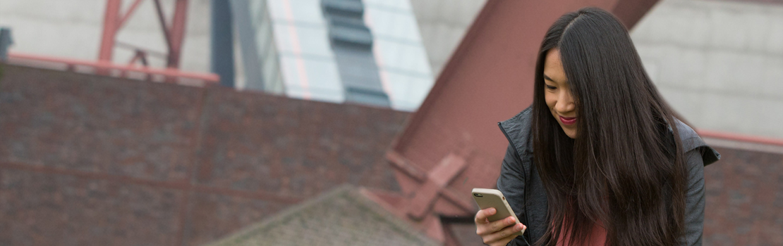 Eine junge Frau schaut konzentriert auf ihr Mobiltelefon, sie sitzt vor der Zeche Zollverein in Essen